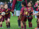 Young Porirua Vikings junior rugby league players in maroon and green uniforms take part in a game on a grass field, with one child running forward carrying the ball.