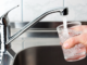Water flows from a household tap into a glass held over a kitchen sink.