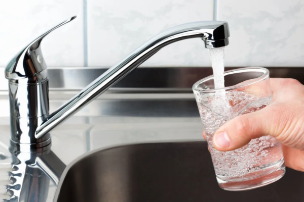 Water flows from a household tap into a glass held over a kitchen sink.