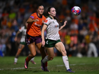Wellington Phoenix defender tracks the ball in mid-air while a Brisbane Roar player pressures from behind during a semi-final match.
