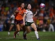 Wellington Phoenix defender tracks the ball in mid-air while a Brisbane Roar player pressures from behind during a semi-final match.