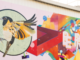 Colourful mural featuring a flying stitchbird with golden wings beside bold rainbow geometric shapes.
