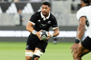 Alt text: All Blacks loose forward Ardie Savea carries the ball during a rugby match, wearing the black New Zealand jersey as an opposing player moves in to defend.