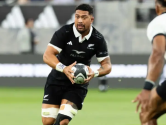 Alt text: All Blacks loose forward Ardie Savea carries the ball during a rugby match, wearing the black New Zealand jersey as an opposing player moves in to defend.