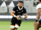 Alt text: All Blacks loose forward Ardie Savea carries the ball during a rugby match, wearing the black New Zealand jersey as an opposing player moves in to defend.