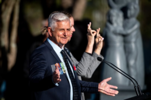 Porirua City Councillor Mike Duncan speaks at an outdoor civic service beside a New Zealand Sign Language interpreter.