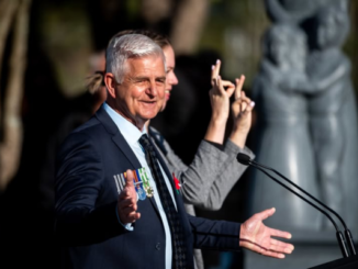 Porirua City Councillor Mike Duncan speaks at an outdoor civic service beside a New Zealand Sign Language interpreter.