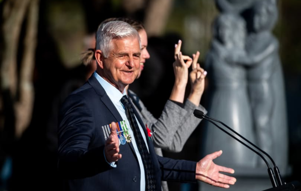 Porirua City Councillor Mike Duncan speaks at an outdoor civic service beside a New Zealand Sign Language interpreter.