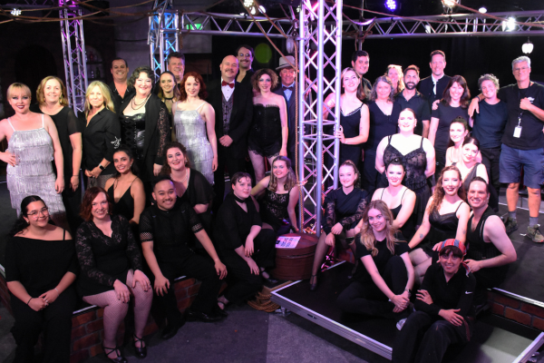 Porirua Little Theatre cast and crew gather on stage under purple and white theatre lighting after a production.