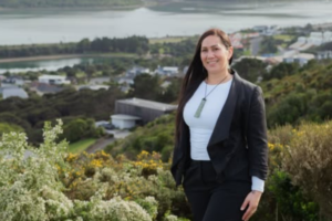 Jessica Tehuia stands on a hillside overlooking Porirua Harbour and nearby buildings.