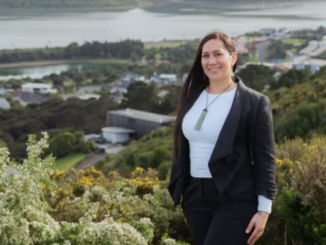 Jessica Tehuia stands on a hillside overlooking Porirua Harbour and nearby buildings.