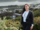 Jessica Tehuia stands on a hillside overlooking Porirua Harbour and nearby buildings.