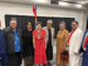 Porirua Mayor Anita Baker stands with Samoan community leaders and guests during a Samoa Language Week and Samoan Independence Day celebration. The group poses for a photo beneath a Samoan flag at an indoor community event.