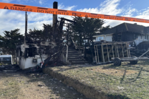 Fire-damaged house in Spur Grove, Tītahi Bay, behind danger tape after a Saturday night blaze.