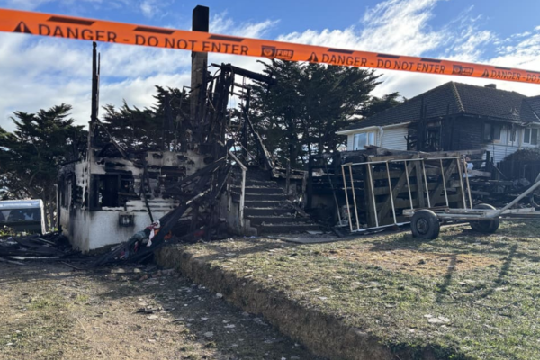 Fire-damaged house in Spur Grove, Tītahi Bay, behind danger tape after a Saturday night blaze.