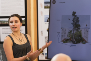 A student presents Te Manawa design concepts beside a screen showing a courtyard proposal.