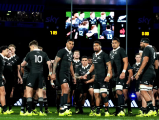All Blacks players gather on the field during a rugby match, with the stadium screen visible in the background.