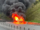 Alt text: A vehicle engulfed in flames on State Highway 1 at Transmission Gully, with thick black smoke rising above the road.