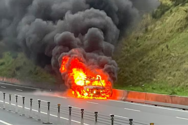 Alt text: A vehicle engulfed in flames on State Highway 1 at Transmission Gully, with thick black smoke rising above the road.