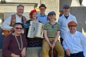 Seven members of the Klezmer Rebs pose together with an accordion, violin and guitar.