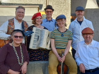 Seven members of the Klezmer Rebs pose together with an accordion, violin and guitar.