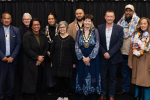 A group of 10 people, some wearing colourful garlands and one wearing a mayoral chain, stand together at the 2026 Porirua Civic Awards.