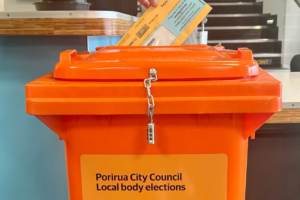 A voting paper being placed into an orange Porirua City Council local body elections ballot box.