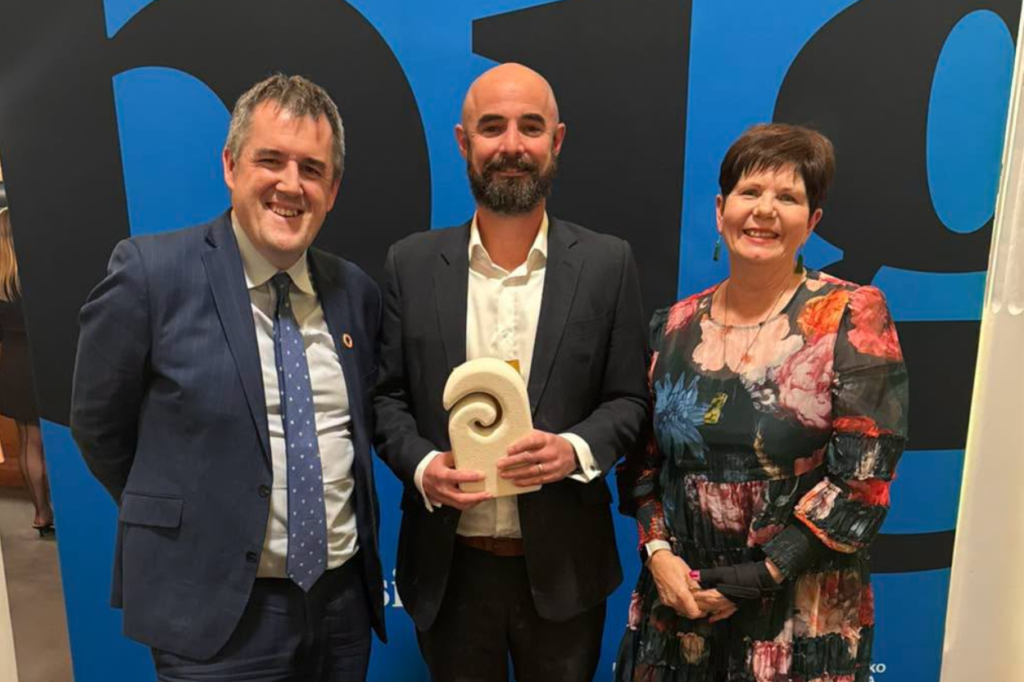 Minister Chris Bishop, Mufftech founder Simon Stone and Porirua Mayor Anita Baker stand together at the Gold Awards, with Stone holding a trophy.