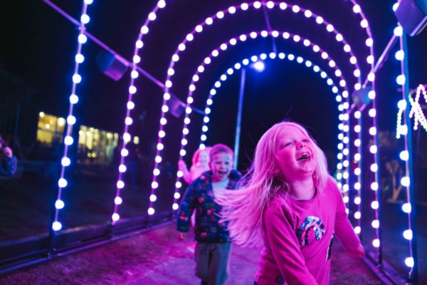 Alt text: Children run through a colourful tunnel of lights at Porirua’s harbourside Matariki light display.