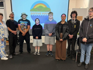 Group photo of Porirua students and an adult standing in front of a projected Porirua Voices Youth Podcast logo at the podcast launch event.