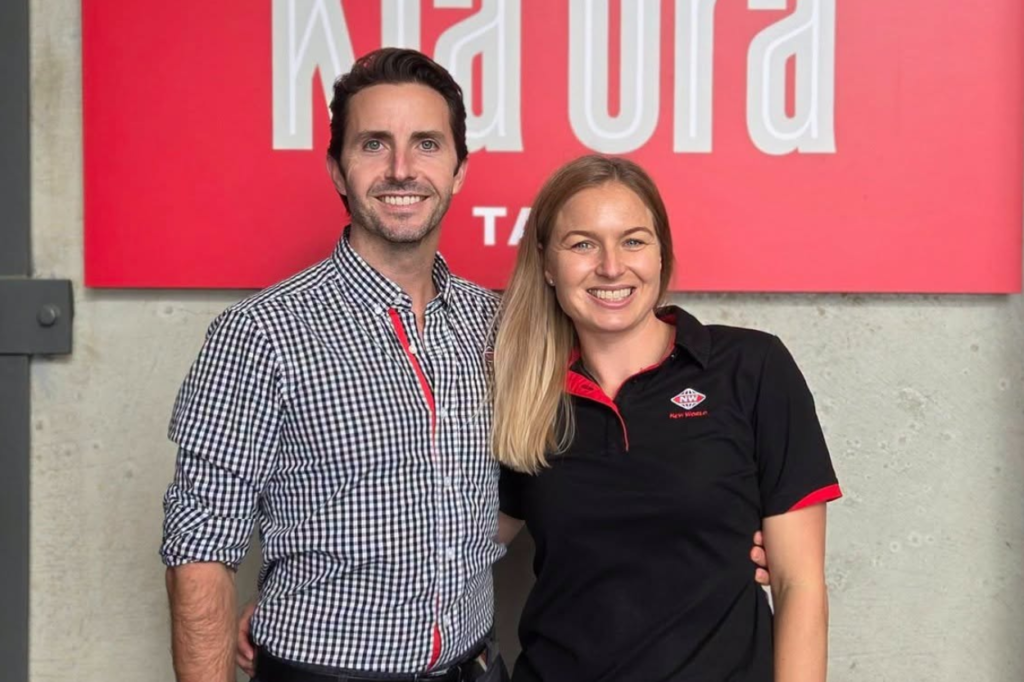 Scott and Ash smiling in front of a New World Tawa sign.