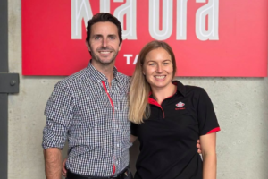 Scott and Ash smiling in front of a New World Tawa sign.