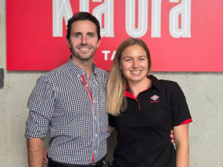Scott and Ash smiling in front of a New World Tawa sign.
