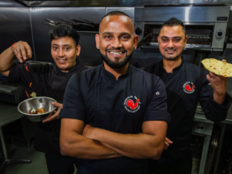 Three Sushil’s Musclechef Café team members in a commercial kitchen, with one holding a pan of food and another holding flatbread.
