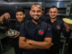 Three Sushil’s Musclechef Café team members in a commercial kitchen, with one holding a pan of food and another holding flatbread.