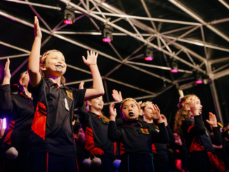Young performers from Ngā Taitāmariki ō Ngāti Pōneke Young Māori Club perform on stage with raised hands.