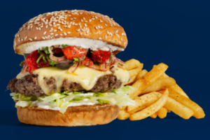 A cheeseburger topped with lettuce, tomato and onion, served with seasoned fries against a dark blue background.