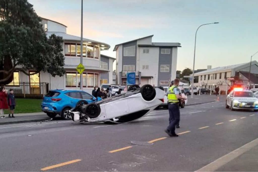 A white car lies upside down on Moorefield Road in Johnsonville as police attend the crash scene.