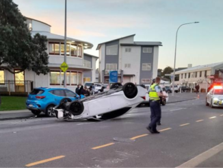 A white car lies upside down on Moorefield Road in Johnsonville as police attend the crash scene.