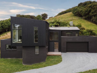 Deviation House in Pāuatahanui, with dark timber cladding, brick walls and a double garage set against a rural hillside.