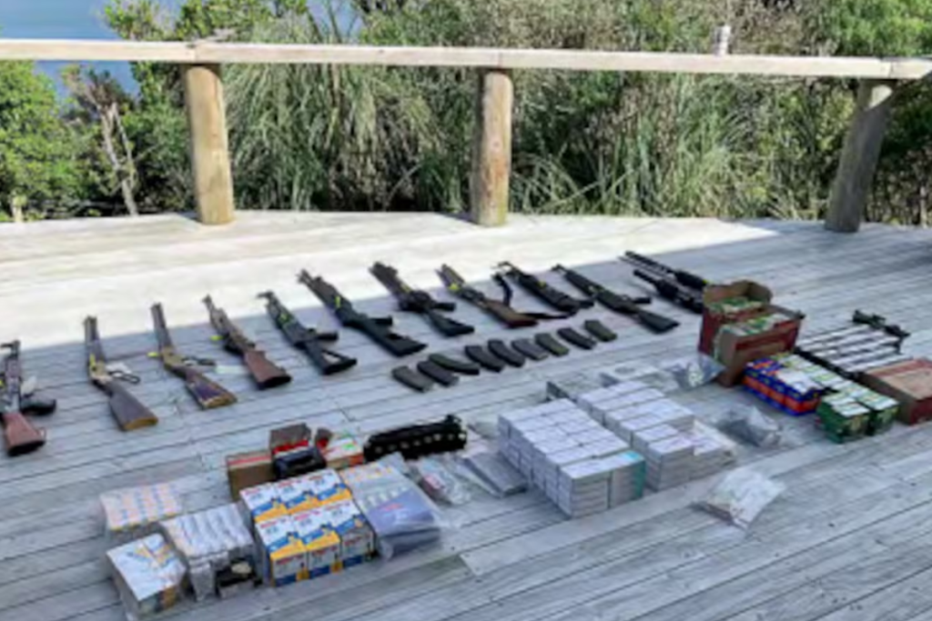 Fifteen firearms, prohibited magazines and boxes of ammunition laid out on a wooden deck after a police search at Crail Bay.