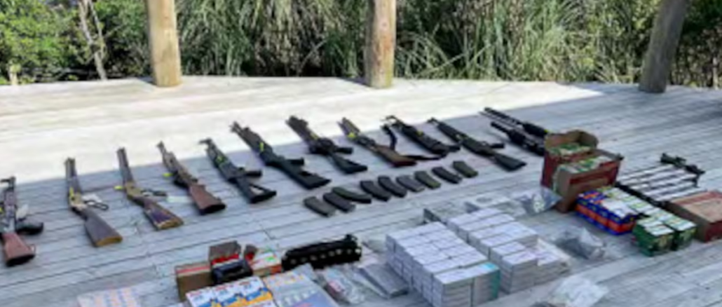 Fifteen firearms, prohibited magazines and boxes of ammunition laid out on a wooden deck after a police search at Crail Bay.