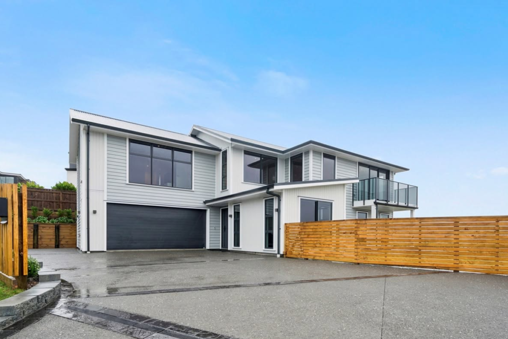 Modern two-storey Porirua home with white and grey cladding, black-framed windows, a double garage, glass balcony and timber fence.