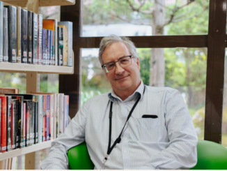 Porirua Libraries Manager Brian Anderson sitting inside a library surrounded by books.
