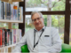 Porirua Libraries Manager Brian Anderson sitting inside a library surrounded by books.