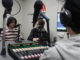 Three young people wearing headphones sit around microphones in a radio studio, with a mixing desk in the foreground.