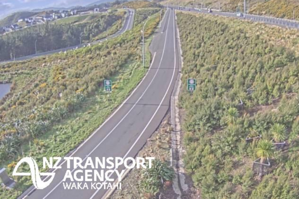 An empty section of divided state highway winding through green hills, with the NZ Transport Agency Waka Kotahi logo in the lower left.