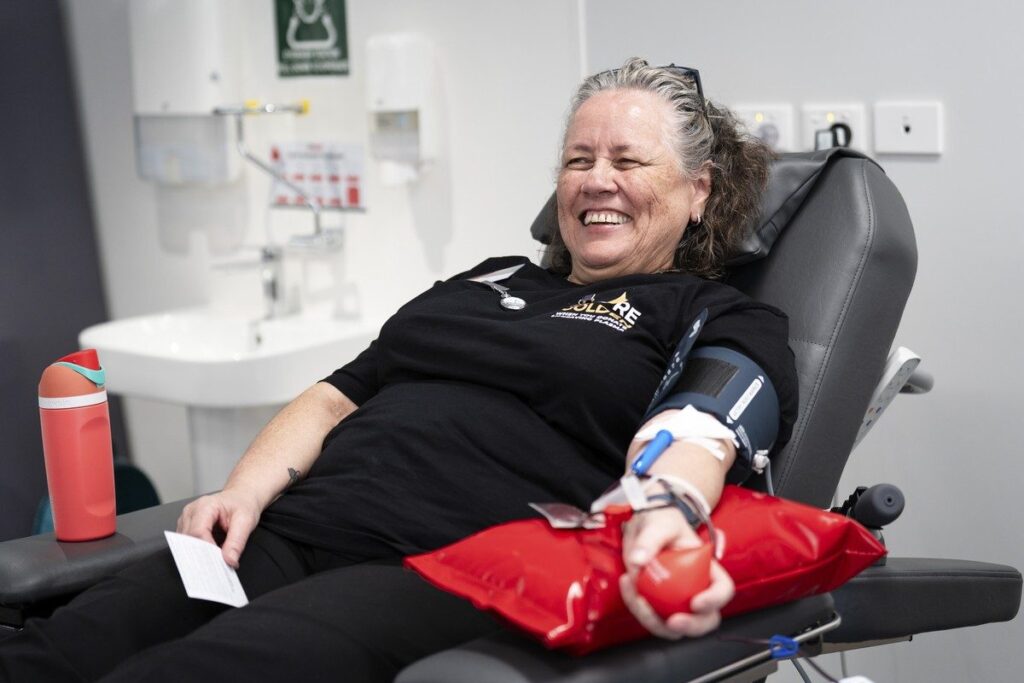 A smiling woman reclines in a donor chair while giving blood.