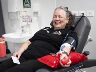 A smiling woman reclines in a donor chair while giving blood.