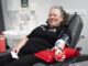 A smiling woman reclines in a donor chair while giving blood.